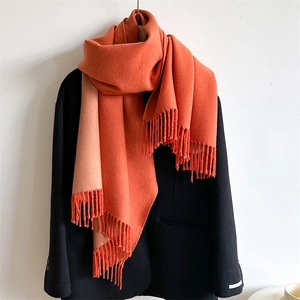 Detail view of double-sided orange and beige scarf with tassel edge on black coat