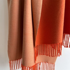 Detail of soft cashmere-like scarf showing orange and brown double-sided fabric with tassels