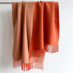 Detail of double-sided cashmere-style scarf showing orange and red tones with fringe edges
