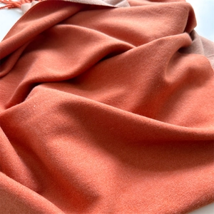 Detail of two-tone orange and beige cashmere scarf with soft texture and fringe edges