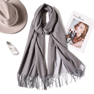 Flat lay of a grey cashmere-style scarf with fringe, styled with a hat and perfume