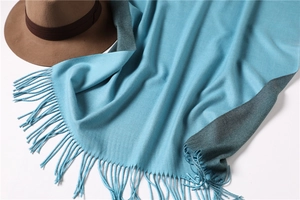 Detail of light blue cashmere-style scarf featuring dark grey piping and long tassels