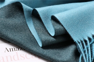 Detailed macro view of soft teal cashmere scarf with fine fabric texture and tassel fringe