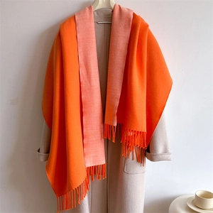 Close-up of vibrant orange scarf with tassels draped over a beige coat for winter style