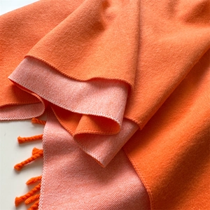 Detail of two-tone orange cashmere-feel scarf showing thick texture and woven tassels
