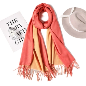 Detailed flat lay of coral and yellow cashmere-feel scarf with elegant fringe and fedora