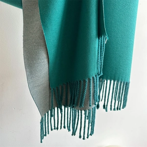 Detail of dual-color knit scarf in peacock green and light gray with fringed edges