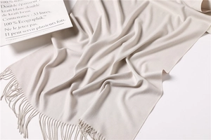 Detail of off-white cashmere-style scarf with fine tassels and premium soft knit texture