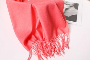 Detail of coral pink cashmere-like scarf showing fine tassel fringe and soft fabric texture