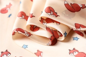 Detail of silk-like satin square scarf featuring cute cartoon fox and blue star patterns