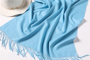 Flat lay of soft light blue cashmere scarf with fine tassel details and stylish hat