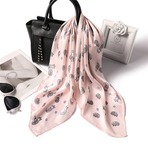 Pink silk-like scarf with cartoon fox and star prints draped over a leather handbag