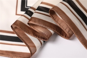 Vista macro di foulard in raso con strisce geometriche e dettagli di orlo rifiniti
