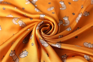 Macro detail of silk-like satin fabric with cute fox and star prints in warm mustard yellow