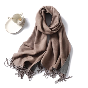 Close-up of double-sided brown and gray scarf with tassels beside a white coffee cup