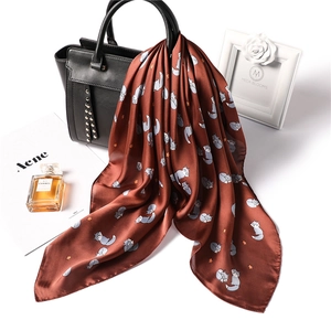 Detail of reddish-brown silk scarf with cartoon fox pattern tied on a luxury leather handbag