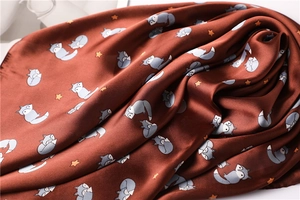 Detail of silk square scarf featuring cute cartoon foxes and stars on brown fabric