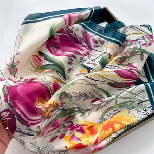 Close-up of floral print silk scarf with teal edges folded in a luxury gift box