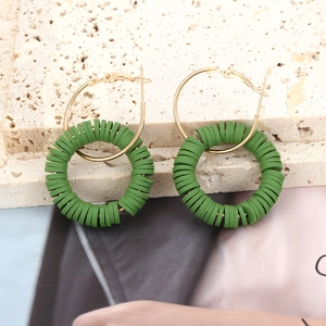 Detail of bohemian gold hoop earrings with green clay discs on a stone pedestal