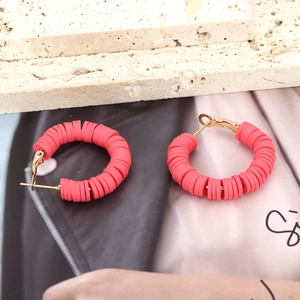 Detailed view of red clay disc hoop earrings with gold-tone hardware on travertine