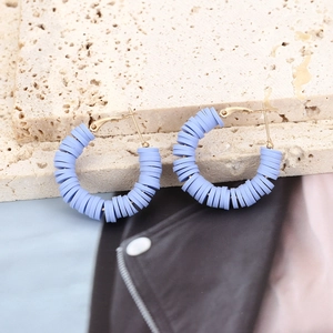 Close-up of light blue bohemian polymer clay disc hoop earrings on a stone display