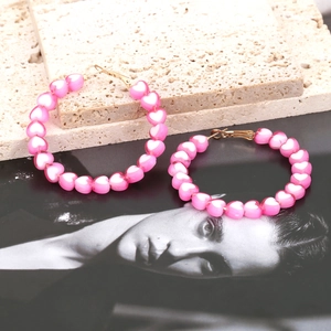 Pink heart bead hoop earrings on a textured stone stand with fashion photography backdrop