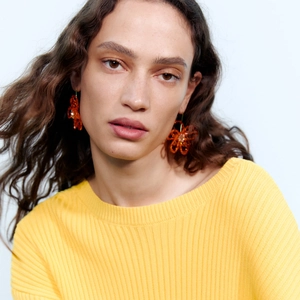Boucles d'oreilles fleurs orange portées par un mannequin en haut en maille