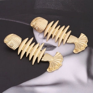 Golden fishbone drop earrings with sparkling rhinestone eye detail on a stylish background