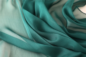Dettaglio del tessuto in seta leggera sfumata verde con drappeggio elegante e texture