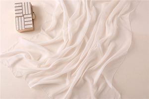 Detalle del chal de gasa crema con costuras finas junto a un bolso de mano de lujo