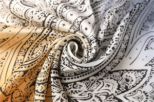 Macro detail of silk-like scarf featuring golden paisley mandala patterns and soft texture