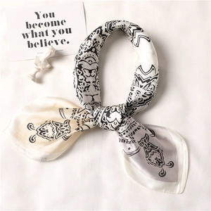 Elegant beige silk-like scarf with black paisley pattern tied in a stylish knot