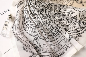 Detailed close-up of soft black and white paisley pattern on silky satin square scarf