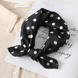 Close-up of black silk scarf with white polka dots styled on a neutral shirt background