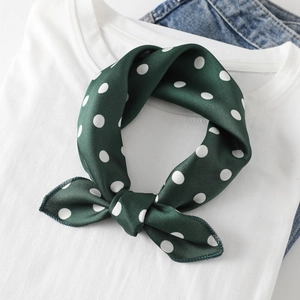 Close-up of a green polka dot silk scarf styled as a neck knot on a denim jacket