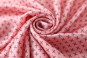 Détail d'un foulard en satin rose montrant la texture lisse et le motif de croix noire