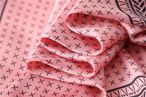 Gros plan d'un foulard en soie rose avec texture lisse et motifs de croix noires élégants