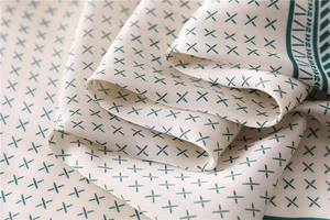 Texture détaillée du foulard en soie avec motif X vert et bordure géométrique élégante