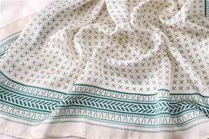 Détail d'un foulard 70x70cm en soie crème avec motifs géométriques bleus et texture soyeuse