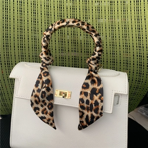 Detail of leopard print silk scarf wrapped on a white pebbled leather handbag handle