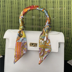 Detail of colorful printed silk scarf wrapped around handle of white textured leather bag