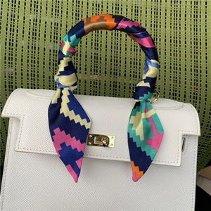 White leather handbag with colorful geometric silk scarf wrapped on the handle and gold lock