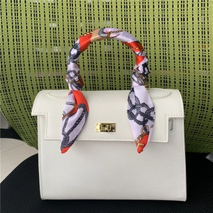 Detail of a white leather handbag handle decorated with a red chain print silk scarf
