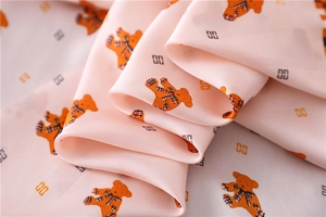 Close-up of soft pink silk fabric featuring teddy bear prints and luxury brand patterns