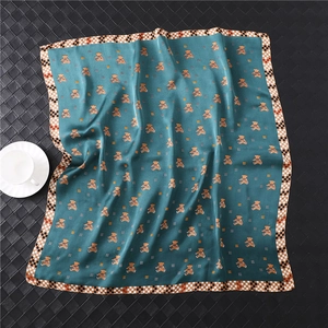 Detail of blue silk scarf with cute bear patterns and checkered border on leather surface