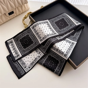 Détail d'un foulard en soie noir et blanc à motif paisley plié sur un plateau chic