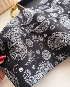Gros plan d'un foulard étroit noir à motif paisley noué sur un sac à main