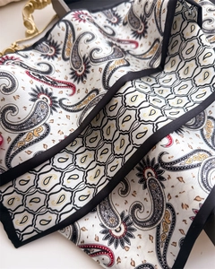 Gros plan d'un foulard en soie paisley avec base ivoire, imprimé et bords roulés noirs