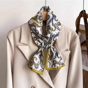 Détail d'un foulard en soie paisley avec bord olive noué sur un revers de blazer beige