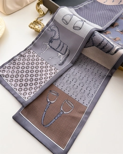Detail of equestrian silk scarf featuring horse motifs, stirrups, and satin finish texture